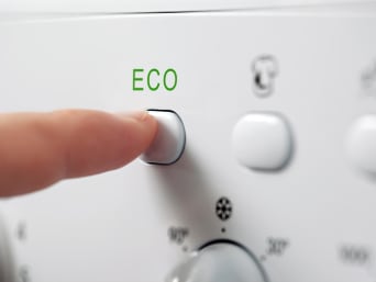Het elektriciteitsverbruik verminderen - Een persoon drukt op het Eco-programma van de wasmachine. Het elektriciteitsverbruik verminderen - Een persoon drukt op het Eco-programma van de wasmachine.