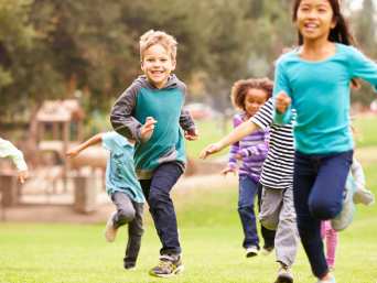 Sport für Kinder: Eine Gruppe von Kindern läuft lachend über eine Wiese. Sport für Kinder: Eine Gruppe von Kindern läuft lachend über eine Wiese.