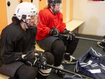 Eishockey Ausrüstung: Zwei Spielerinnen sitzen in ihrer Eishockey-Ausrüstung in der Umkleide. Eishockey Ausrüstung: Zwei Spielerinnen sitzen in ihrer Eishockey-Ausrüstung in der Umkleide.