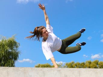 Parkour als Sport: Eine junge Frau springt über eine Mauer. 
