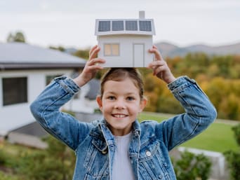Hernieuwbare energie uitgelegd aan kinderen - meisje met een model van een huis met zonnepanelen. Hernieuwbare energie uitgelegd aan kinderen - meisje met een model van een huis met zonnepanelen.