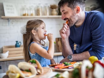 Klimaatvriendelijk eten: vader en dochter eten wortels tijdens het koken. Klimaatvriendelijk eten: vader en dochter eten wortels tijdens het koken.