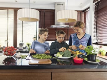 Klimaatvriendelijke voeding: moeder en zonen koken samen met verse ingrediënten. Klimaatvriendelijke voeding: moeder en zonen koken samen met verse ingrediënten.