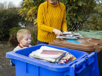 Afval correct scheiden: kleine jongen kijkt in een papierbak. Afval correct scheiden: kleine jongen kijkt in een papierbak.