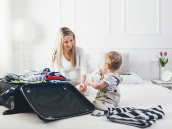 Packliste Ferien – Kleines Kind schaut Mutter beim Kofferpacken zu. Packliste Ferien – Kleines Kind schaut Mutter beim Kofferpacken zu.
