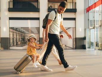 Vliegen met kinderen: klein meisje zit op een koffer op de luchthaven.
