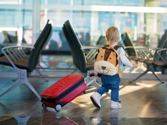 Vliegreizen met kinderen: kleine jongen met rugzak en kinderkoffer. 
