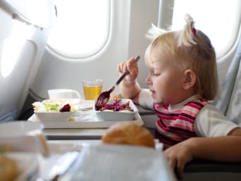 Vliegreizen met kinderen: Klein meisje eet in het vliegtuig.