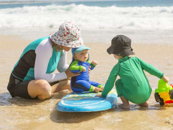 Packliste Sommerurlaub – Mutter, Baby und Kleinkind mit Sonnenhüten spielen am Strand. Packliste Sommerurlaub – Mutter, Baby und Kleinkind mit Sonnenhüten spielen am Strand.