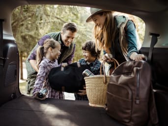 Packliste Familienurlaub – Familie holt das Gepäck aus dem Auto. Packliste Familienurlaub – Familie holt das Gepäck aus dem Auto.