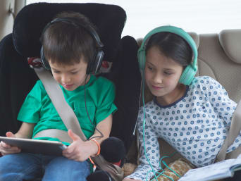 Kinderen gebruiken in de auto een tablet en koptelefoons Kinderen gebruiken in de auto een tablet en koptelefoons