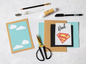 Materials for a Father's Day card with superhero logo.