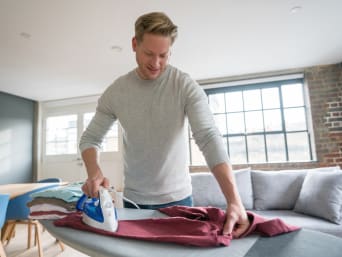 A man ironing a shirt on an ironing board. A man ironing a shirt on an ironing board.