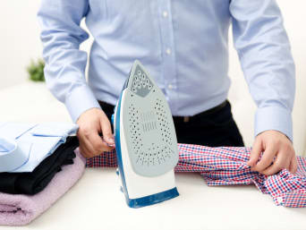 A man ironing a shirt on an ironing board.  A man ironing a shirt on an ironing board.