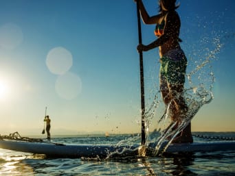 Stand Up Paddle: Zwei Personen paddeln im Sonnenschein auf ihrem SUP-Board über einen See.  Stand Up Paddle: Zwei Personen paddeln im Sonnenschein auf ihrem SUP-Board über einen See.