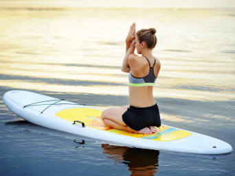 SUP Yoga: Eine Sportlerin macht Yoga-Übungen auf einem stabilen SUP-Board. SUP Yoga: Eine Sportlerin macht Yoga-Übungen auf einem stabilen SUP-Board.