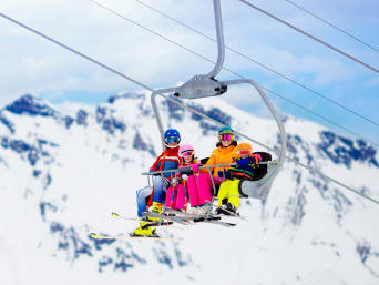Winterurlaub mit Kindern: Familie fährt mit einem Skilift den Berg hinauf. Winterurlaub mit Kindern: Familie fährt mit einem Skilift den Berg hinauf.