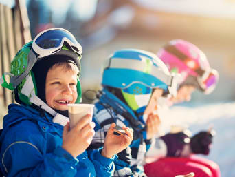 Familienfreundliche Skigebiete: Kinder in Skikleidung genießen eine Pause im Schnee. Familienfreundliche Skigebiete: Kinder in Skikleidung genießen eine Pause im Schnee.