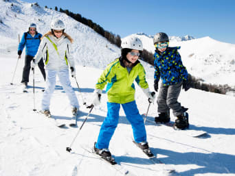 Winterurlaub mit Kindern: Familie auf Skiern fährt einen Hang herunter. Winterurlaub mit Kindern: Familie auf Skiern fährt einen Hang herunter.
