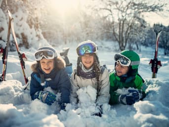 Familienfreundliche Skigebiete: Kinder in Skikleidung liegen glücklich im Schnee. Familienfreundliche Skigebiete: Kinder in Skikleidung liegen glücklich im Schnee.
