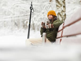 Günstiger Skiurlaub: Junge Frau macht eine Pause beim Skifahren und trinkt aus einer Thermoskanne. Günstiger Skiurlaub: Junge Frau macht eine Pause beim Skifahren und trinkt aus einer Thermoskanne.