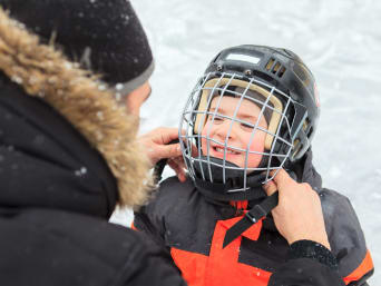 Eishockey Ausrüstung: Vater hilft seinem Sohn, den Helm für das Eishockey-Traning zu veschließen. Eishockey Ausrüstung: Vater hilft seinem Sohn, den Helm für das Eishockey-Traning zu veschließen.