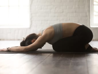Vrouw in de Balasana yogapositie knielt op een yogamatje. Vrouw in de Balasana yogapositie knielt op een yogamatje.